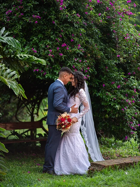 Foto ilustrando um casal no dia de seu casamento sob a sobra de um ambiente arborizado compartilhando um beijo, demonstrando a qualidade e composição das fotografias profissionais oferecidas pela ASH Decorações.